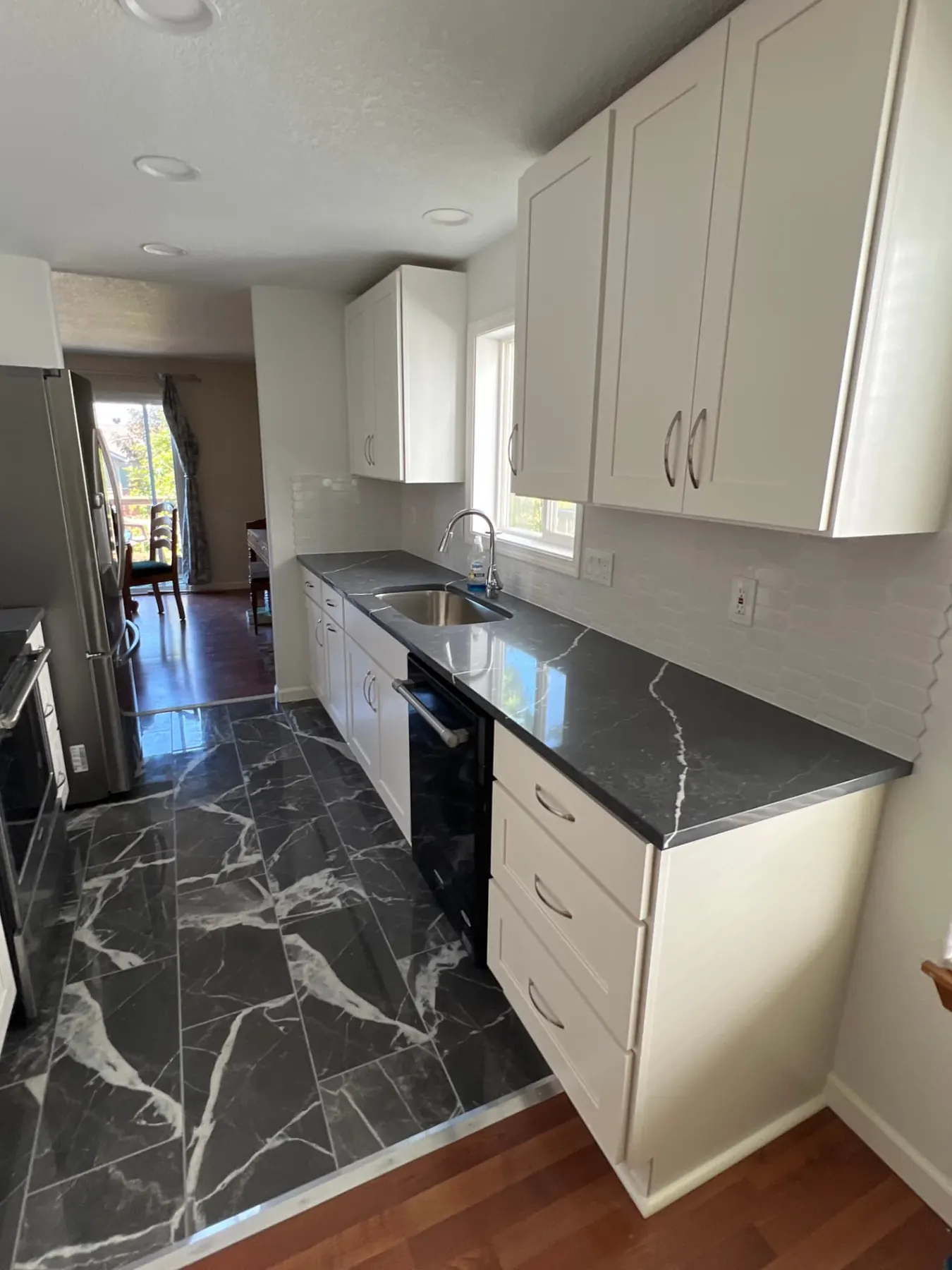 Galley kitchen remodel with dark quartz counters, white shaker cabinets, and marble-look tile floor