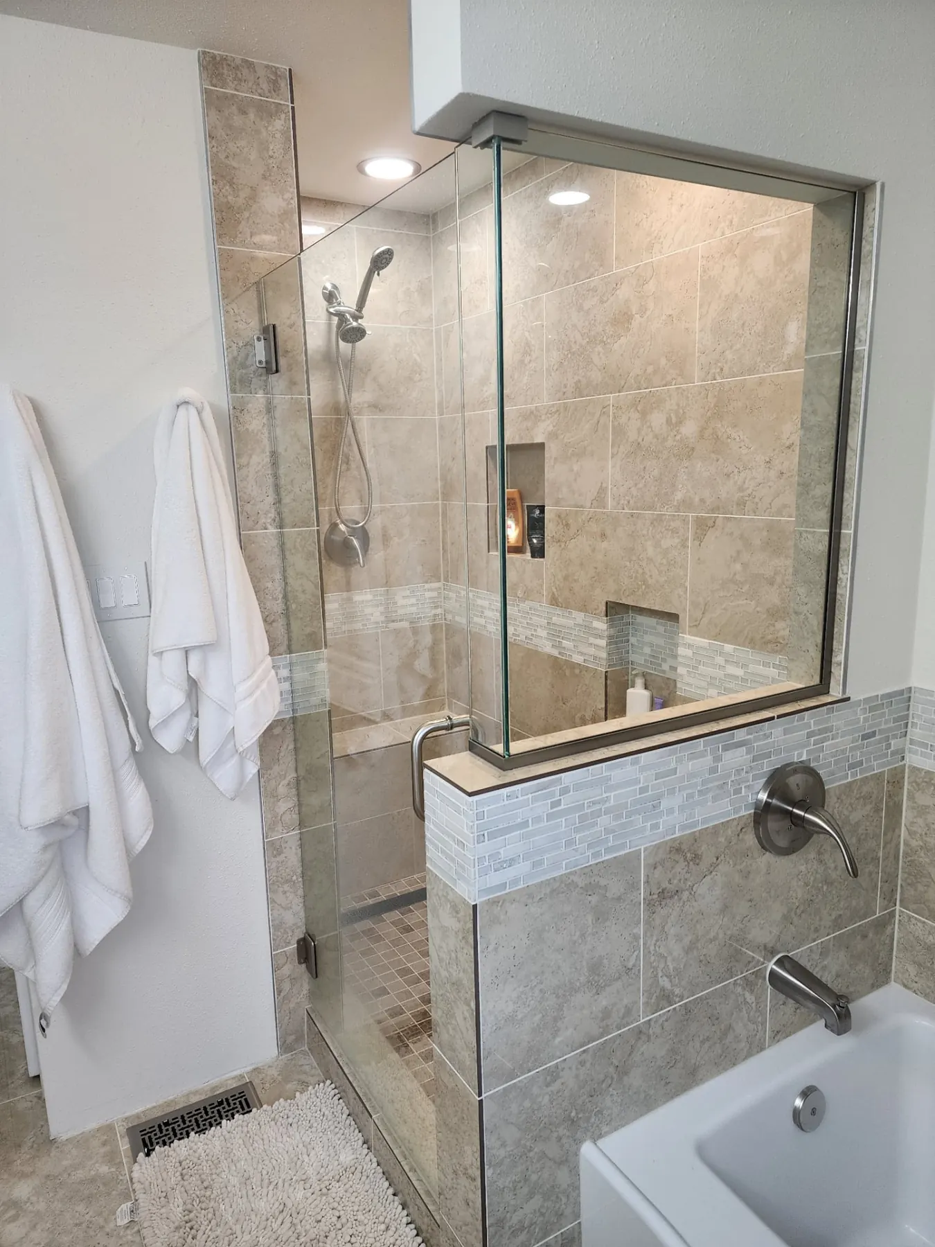 Travertine tile walk-in glass shower with mosaic accent band and soaking tub